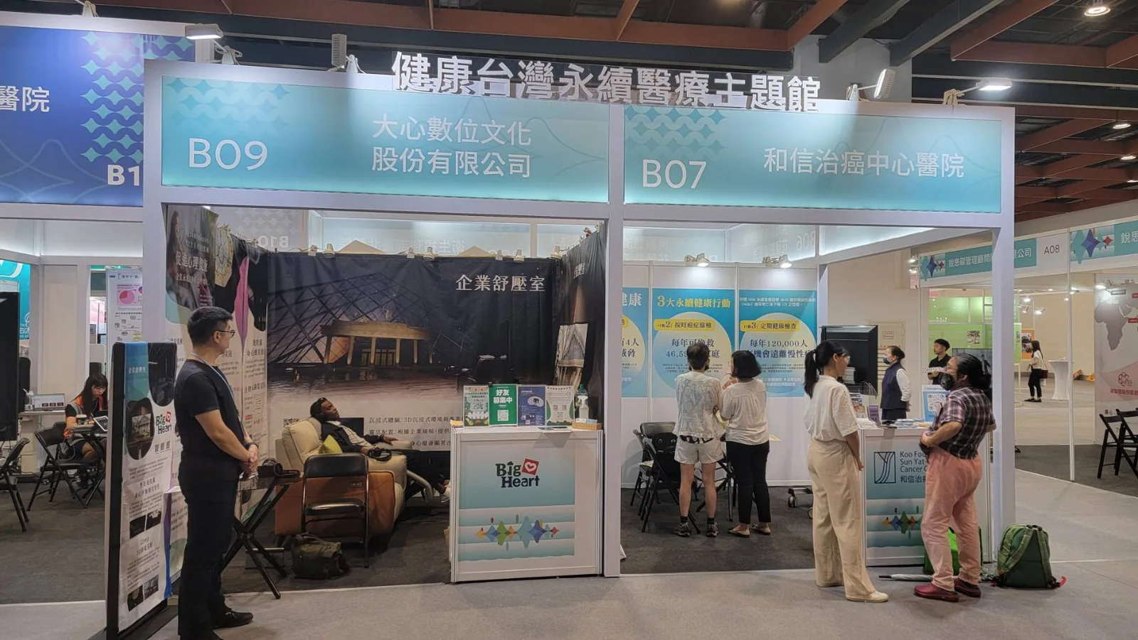 健康台灣永續醫療主題館的 B09 大心數位文化展位:企業舒壓室布置,一位參觀者戴著耳機躺在躺椅上體驗 3D 場景